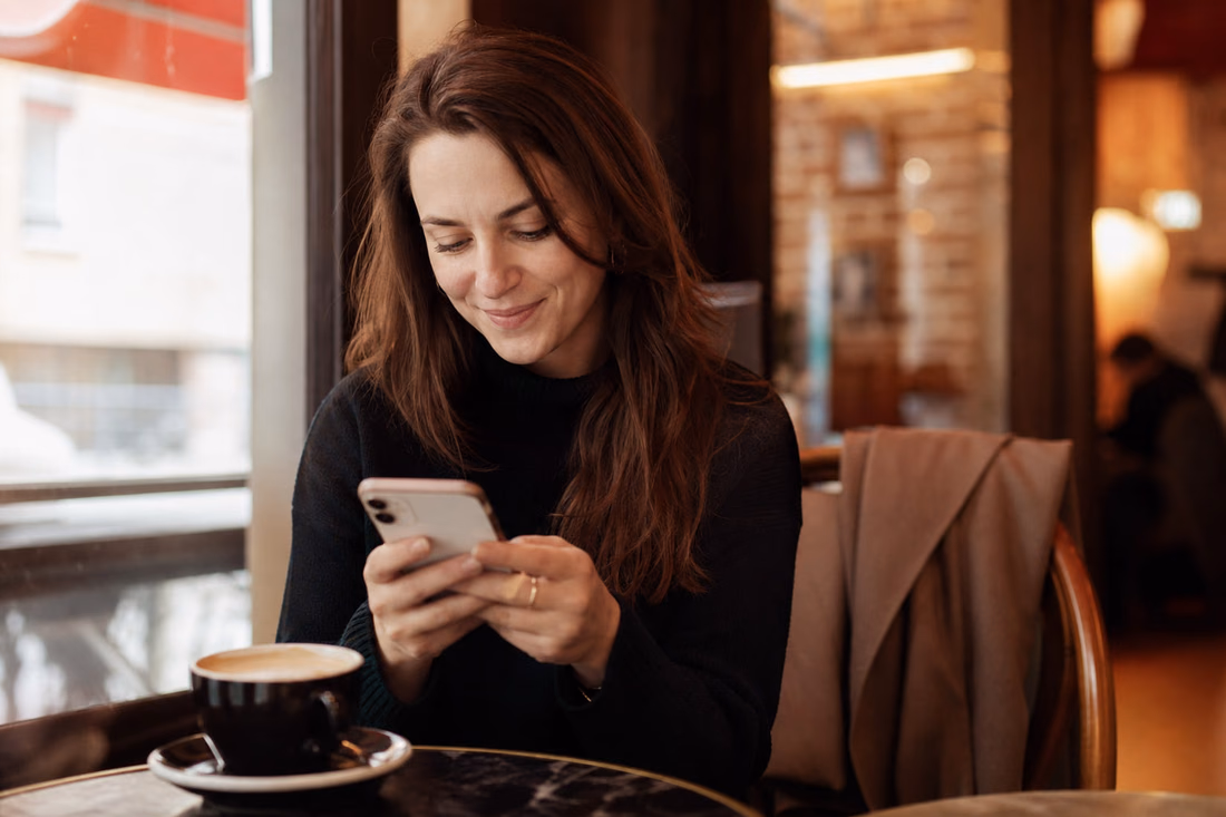 Une femme lit un message sur son téléphone à la table d’un café.