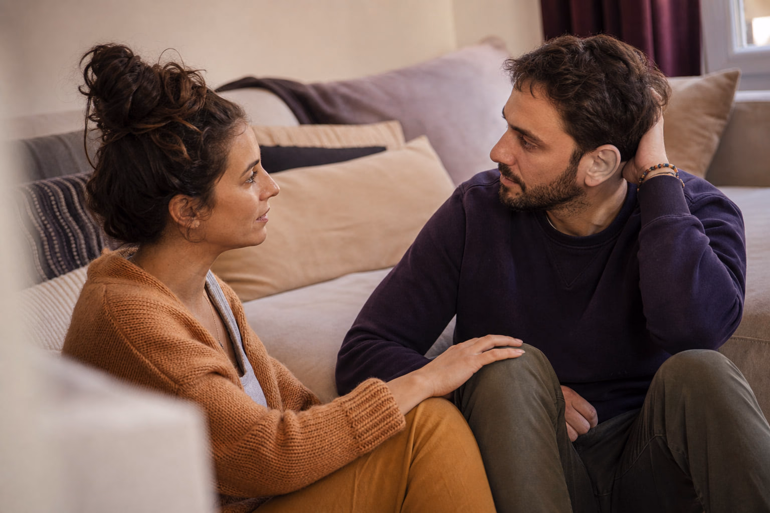 Un couple assis par terre dans son salon, en pleine conversation attentive.