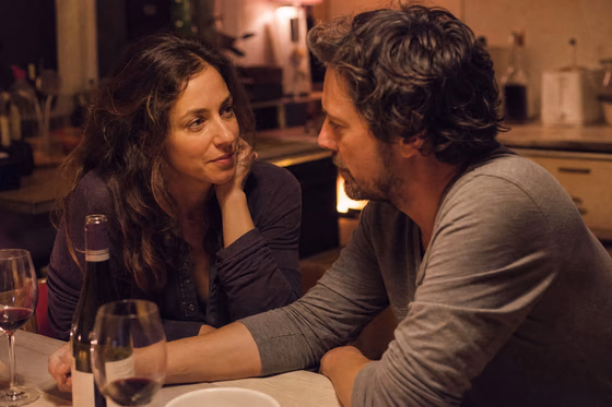Un couple discute longuement à la table de la cuisine, le soir, dans une lumière chaude.