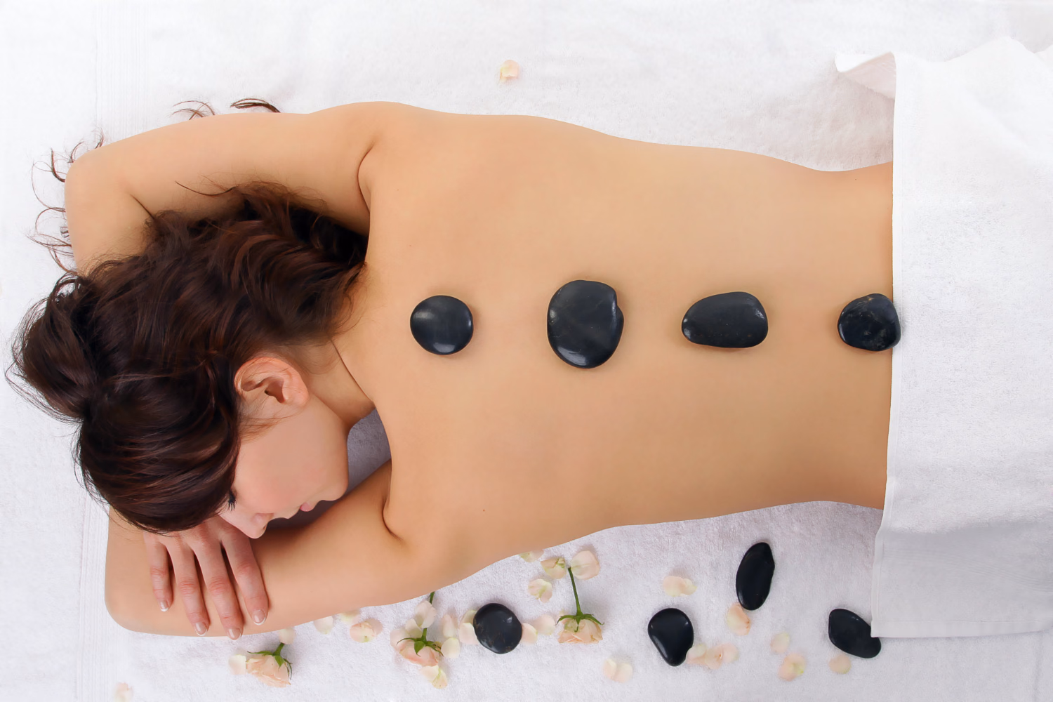 Des pierres chaudes alignées le long du dos d’une personne allongée sur une table de massage.