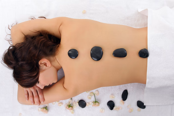 Des pierres chaudes alignées le long du dos d’une personne allongée sur une table de massage.