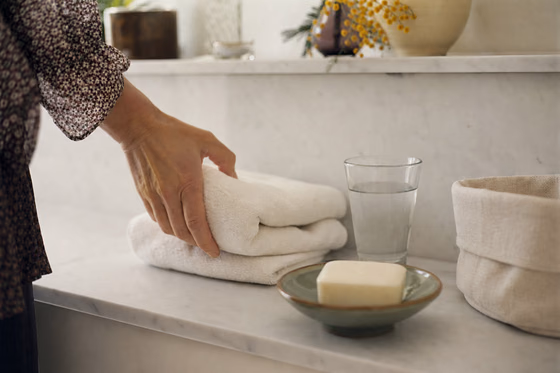 Une étagère de salle de bain avec serviette pliée, savon non parfumé et pochette de rangement.