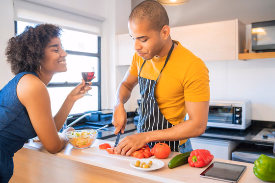Un couple prépare un repas ensemble dans sa cuisine, un verre de vin posé sur le plan de travail.