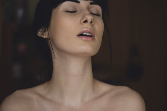 Portrait rapproché d’une femme, tête renversée et yeux fermés, dans une lumière tamisée.