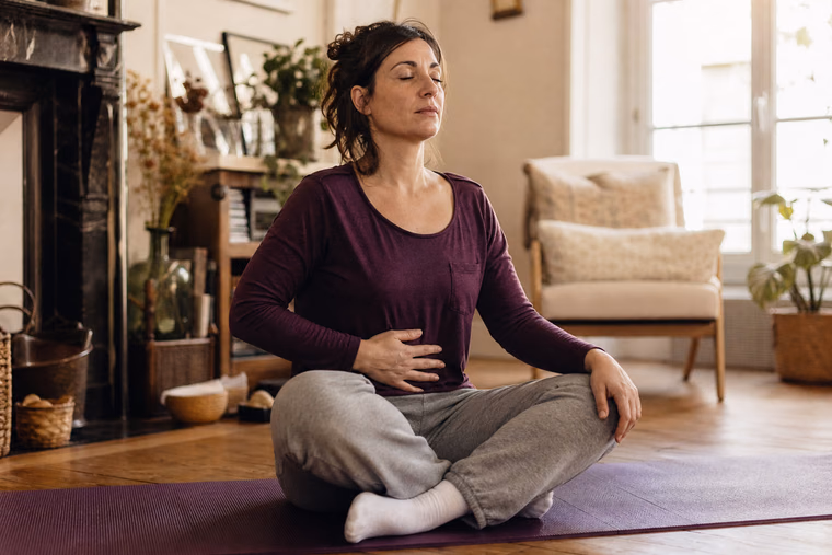 Une femme en tenue de sport respire calmement, assise en tailleur sur un tapis.
